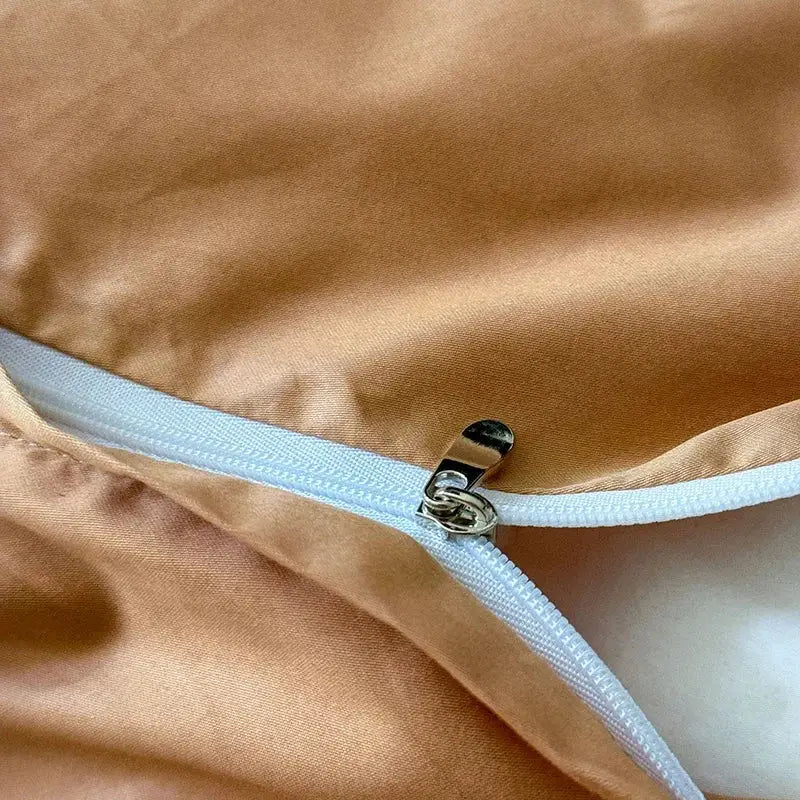 A white zipper with metallic pull on golden-brown satin fabric of floral cream and caramel egyptian cotton bedding set