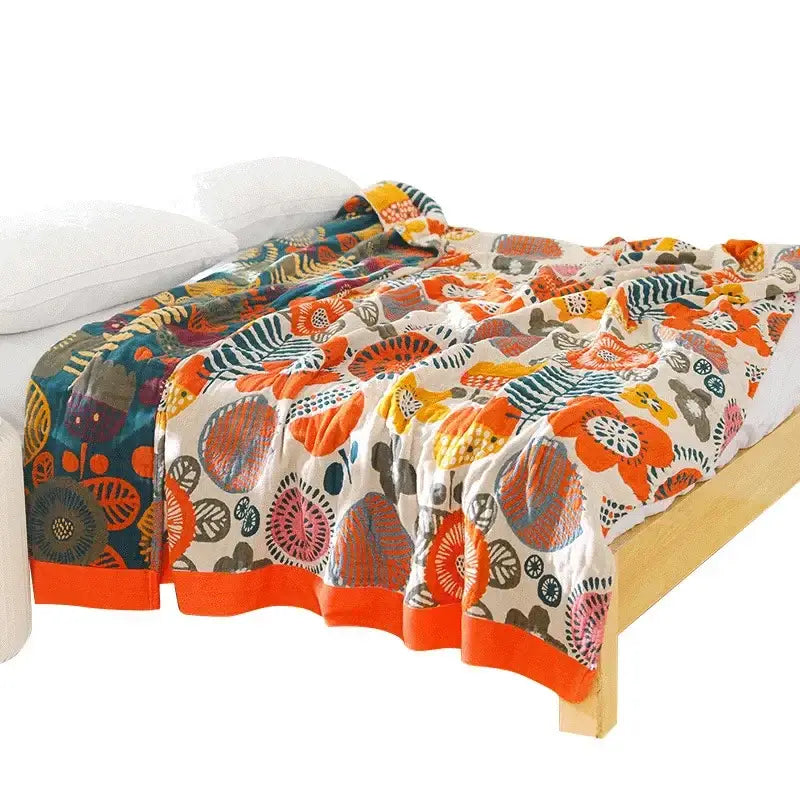 A vibrant floral cream double gauze cotton summer blanket with bold orange and teal designs and an orange hem