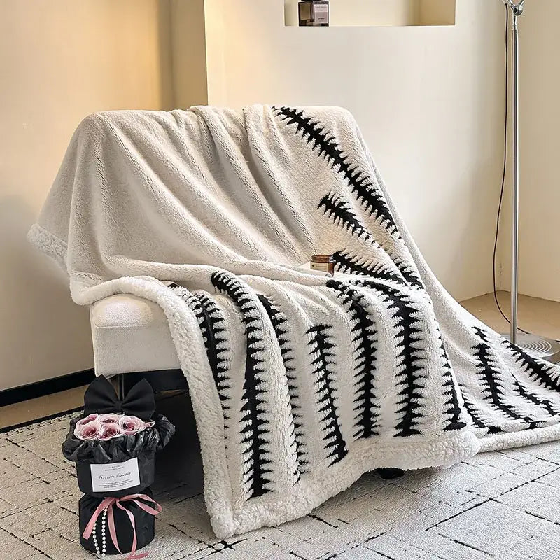 A plush white and black floral cream jacquard lamb wool blanket draped over an armchair with a soft textured surface