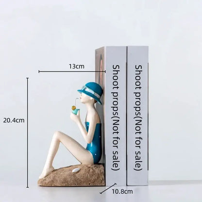 Blue and white resin figure sculpture of a woman in swimsuit sitting on sand holding a drink for living room decor
