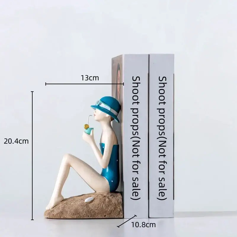 Blue and white resin figure sculpture of a woman in swimsuit sitting on sand holding a drink for living room decor