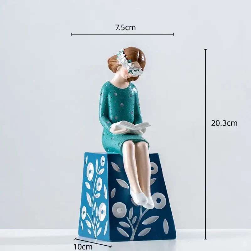 Teal polka-dotted resin figure sculpture of a seated woman with white floral crown holding an open book for living room decor