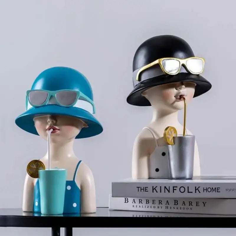 Two stylized resin figure sculptures with floral crowns in teal and black sipping drinks for living room decor