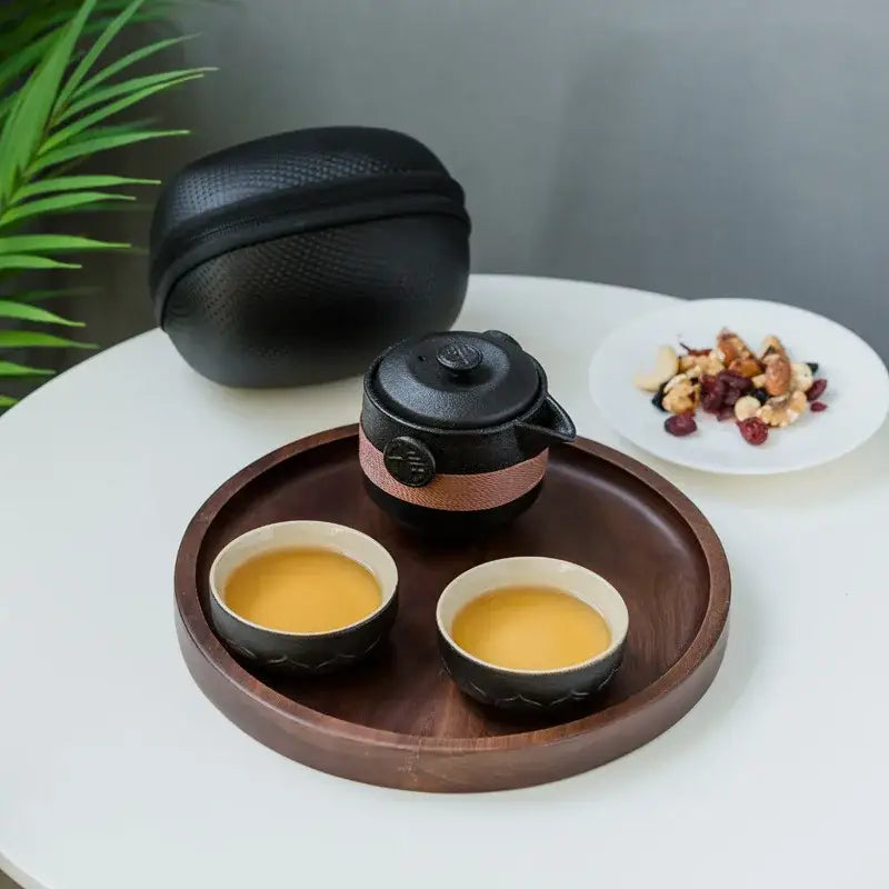 Floral embossed black pottery tea set with copper accent band on dark wood tray with two cups of golden tea decorbites black pottery