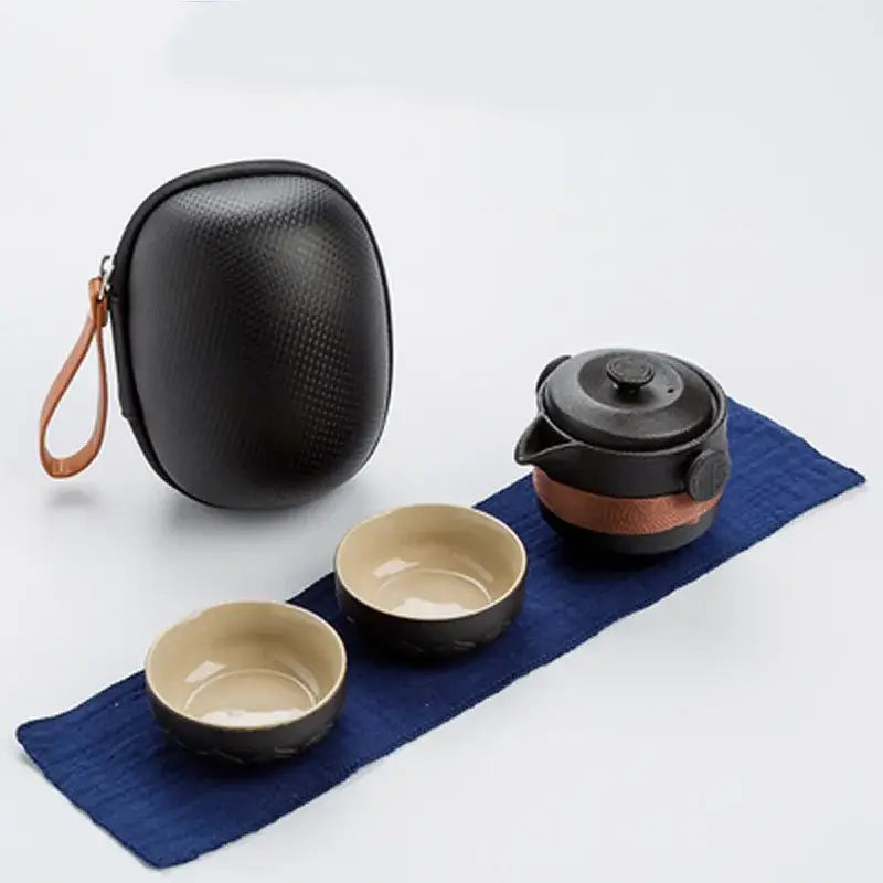 Black ceramic tea set with beige interior and brown leather accents accompanied by textured carrying case decorbites black pottery