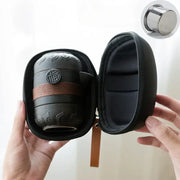 Black pottery tea set with embossed floral patterns and circular chinese emblem secured by brown woven strap travel bag