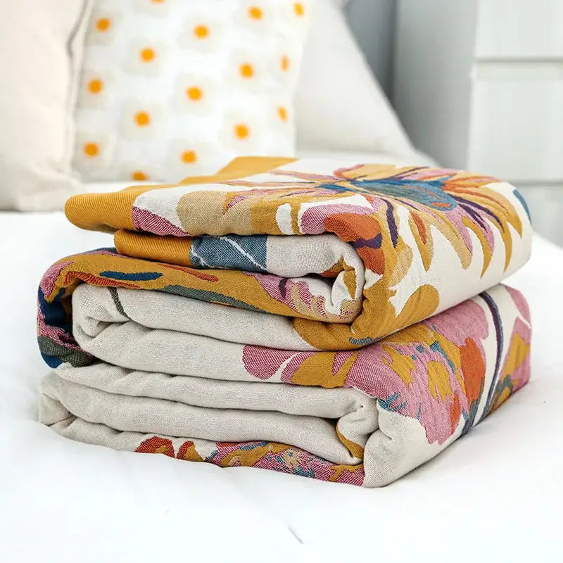 Stack of folded floral embroidered cream and navy cozy gauze cotton throw blankets with vibrant patterns for decorbites cozy gauze