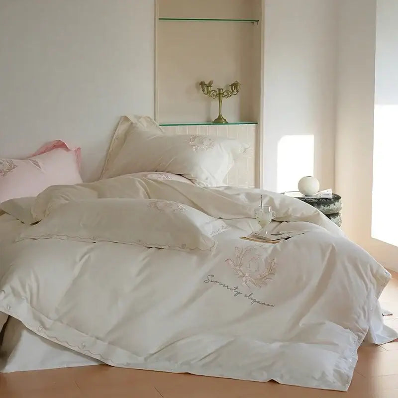 Cream-colored satin duvet cover set with delicate pink floral embroidery and serenity by elegance script detail
