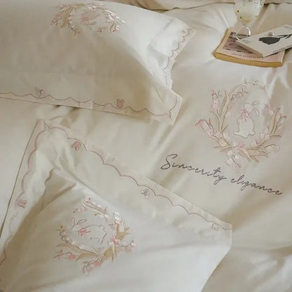 Cream-colored satin duvet cover set with delicate pink and gold floral embroidery and scalloped edges for bedroom decor