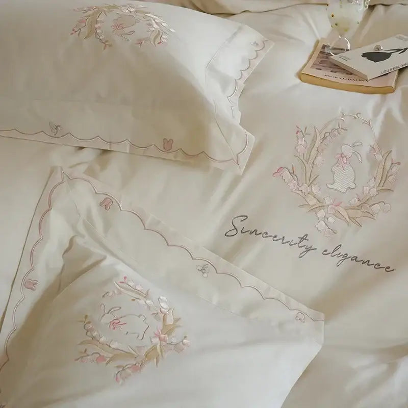 Cream-colored satin duvet cover set with delicate pink and gold floral embroidery and scalloped edges for bedroom decor