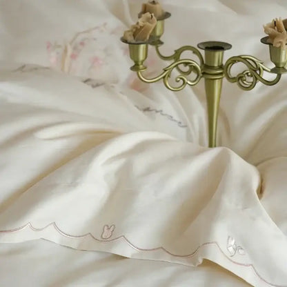 Ivory satin pillowcase with scalloped edges and silver embroidered bunny motifs in floral embroidered cream duvet cover set