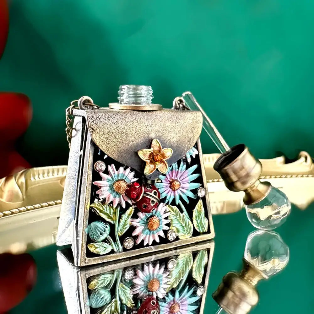 Decorative silver-toned enamel perfume bottle shaped like a handbag with colorful flowers and rhinestones for decor