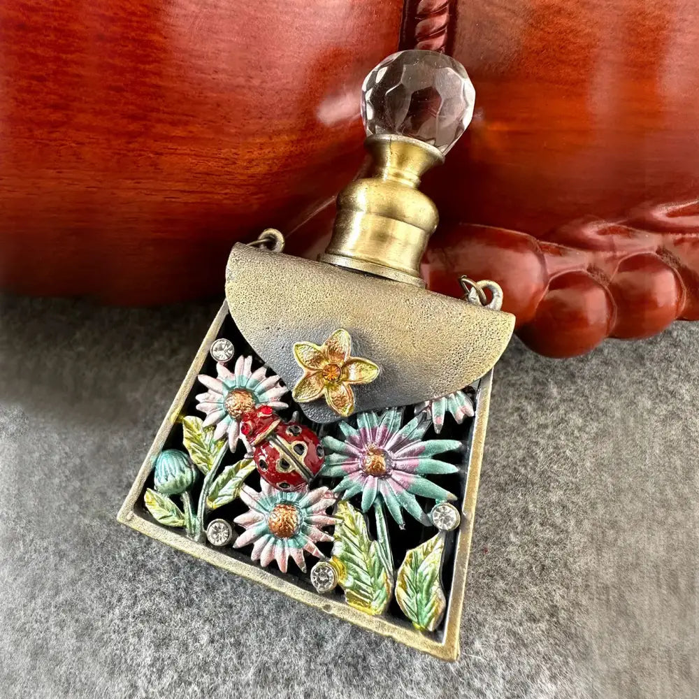 A gold-toned metal enamel perfume bottle pendant with colorful floral rhinestones from a metal handicraft collection