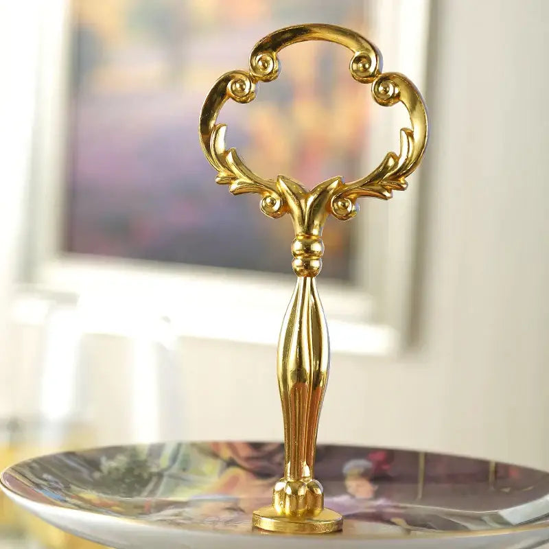 Golden ornate serving handle with intricate scrollwork on a floral gold bone china fruit plates set tiered stand