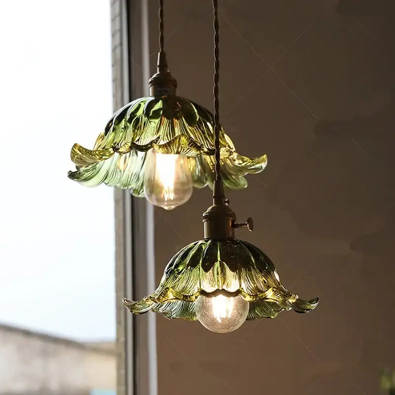Two green glass pendant lights with leaf-shaped design and brass fixtures for dining room lighting