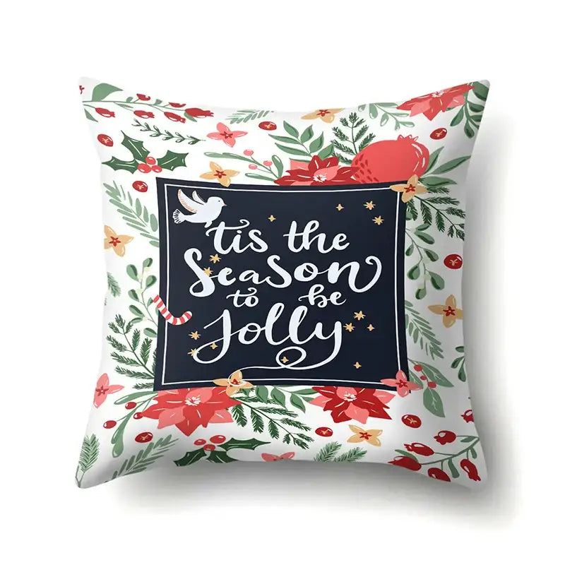 A festive white pillow cover with green tropical leaves and red poinsettias featuring a navy ‘tis the season’ design