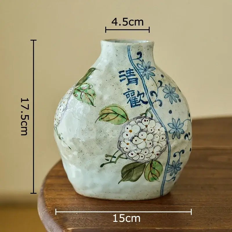 Floral hand painted decorbites ceramic vase with textured off-white glaze and blue floral patterns holding artificial flowers