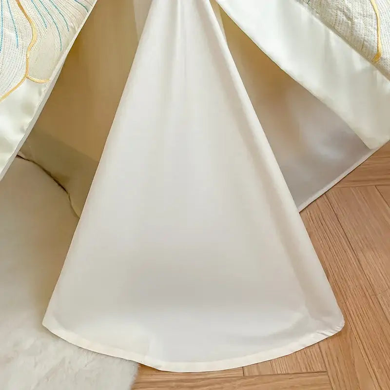 A floral ivory embroidered egyptian cotton bedding set featuring flowing white satin fabric draped over a bed edge