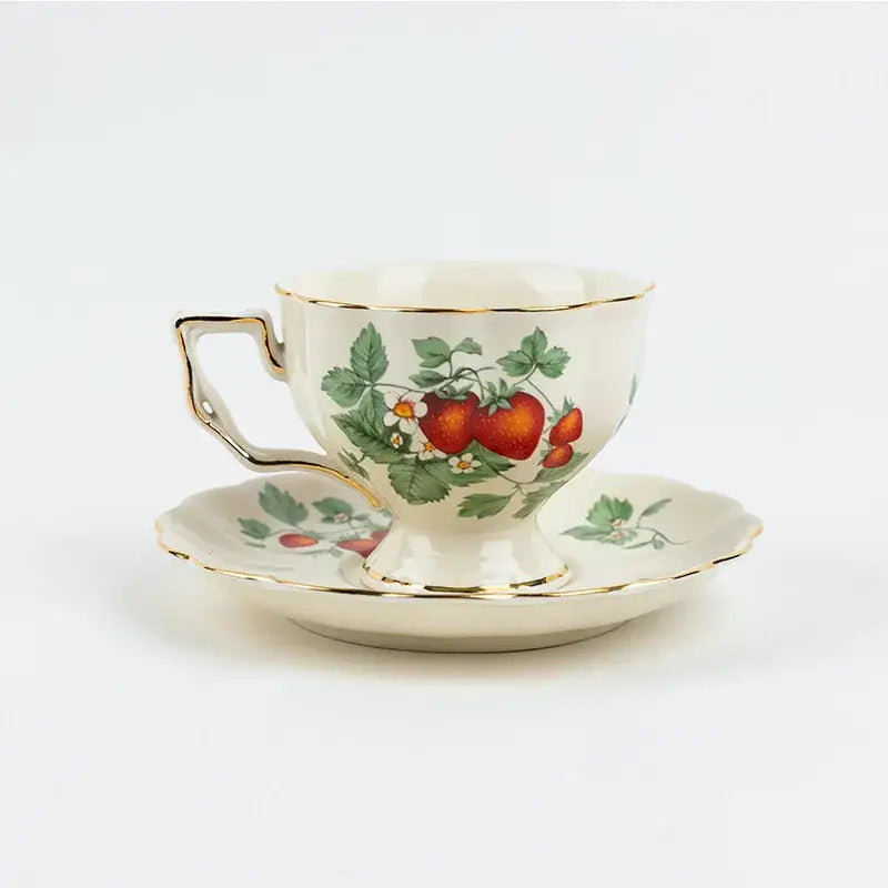 Cream-colored porcelain tea set with gold trim and strawberry motif on teacup and matching saucer for dining room use