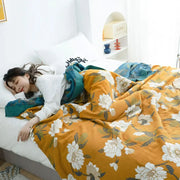 Warm mustard-yellow floral decorbites cotton throw blanket draped over sleeping person in cozy bedroom setting