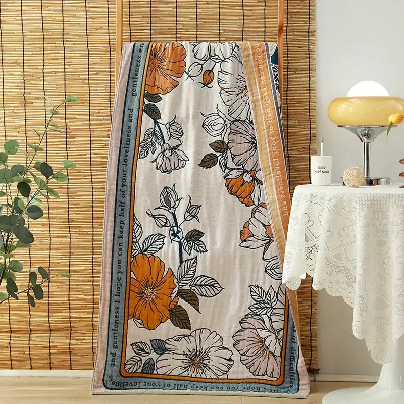 A cream-colored decorbites cotton gauze adult bath towel with vibrant orange and white floral pattern for bedroom decor
