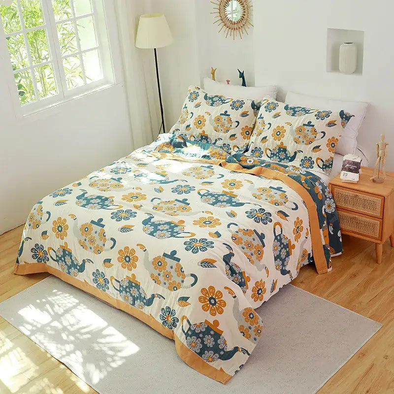 Cream-colored quilted decorbites cotton gauze towel blanket with teal and mustard-yellow teapots and floral pattern border