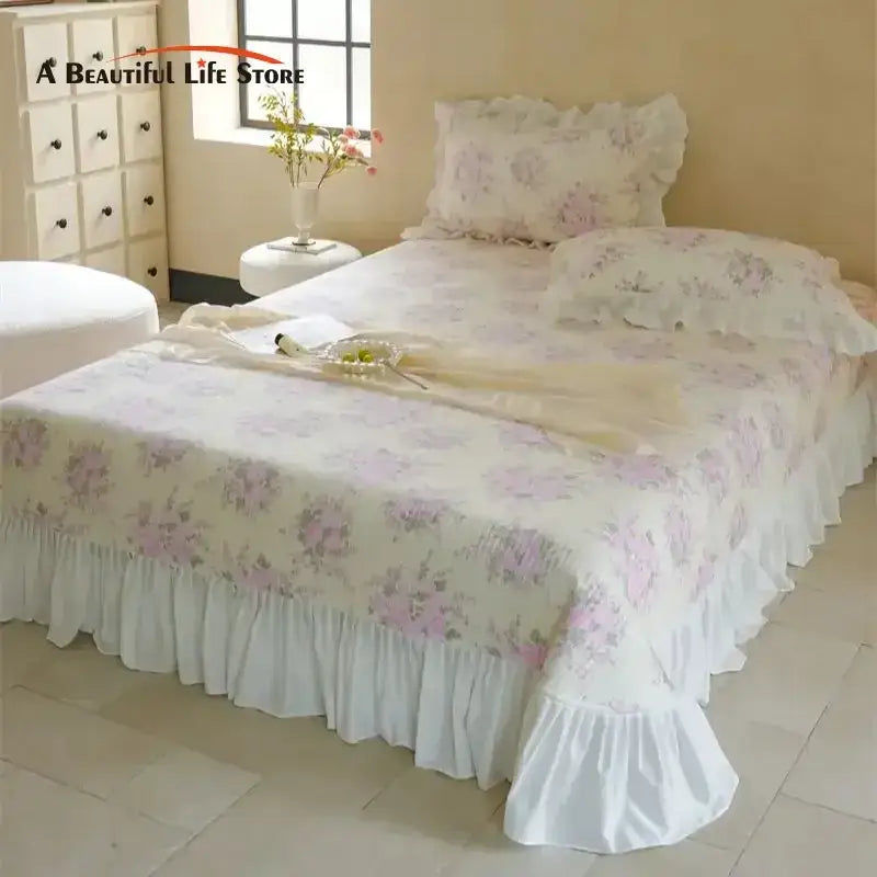 A delicate white quilted bedspread set with soft pink floral patterns and a ruffled hemline for bedroom decor