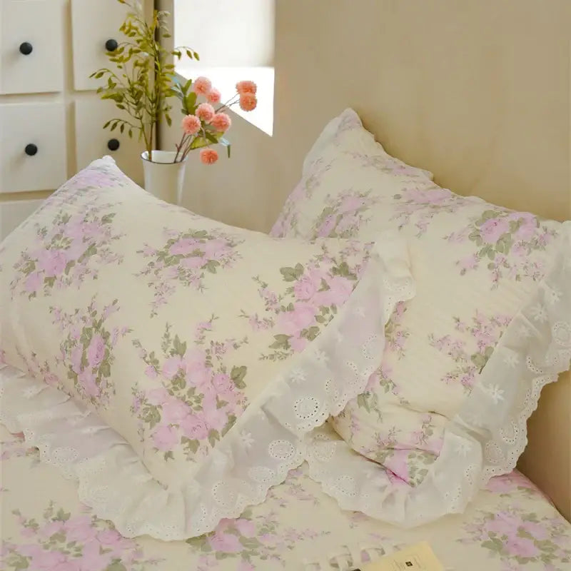 Cream-colored pillowcases with pink green floral patterns and lace trim in a floral pink and white quilted bedspread set