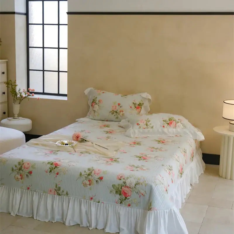 A delicate light blue quilted bedspread set with soft pink roses green leaves and a ruffled edge for bedroom decor