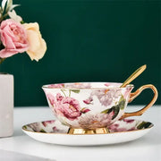 Elegant floral pink and purple porcelain tea cup set with gold-trimmed rim and handle on matching saucer