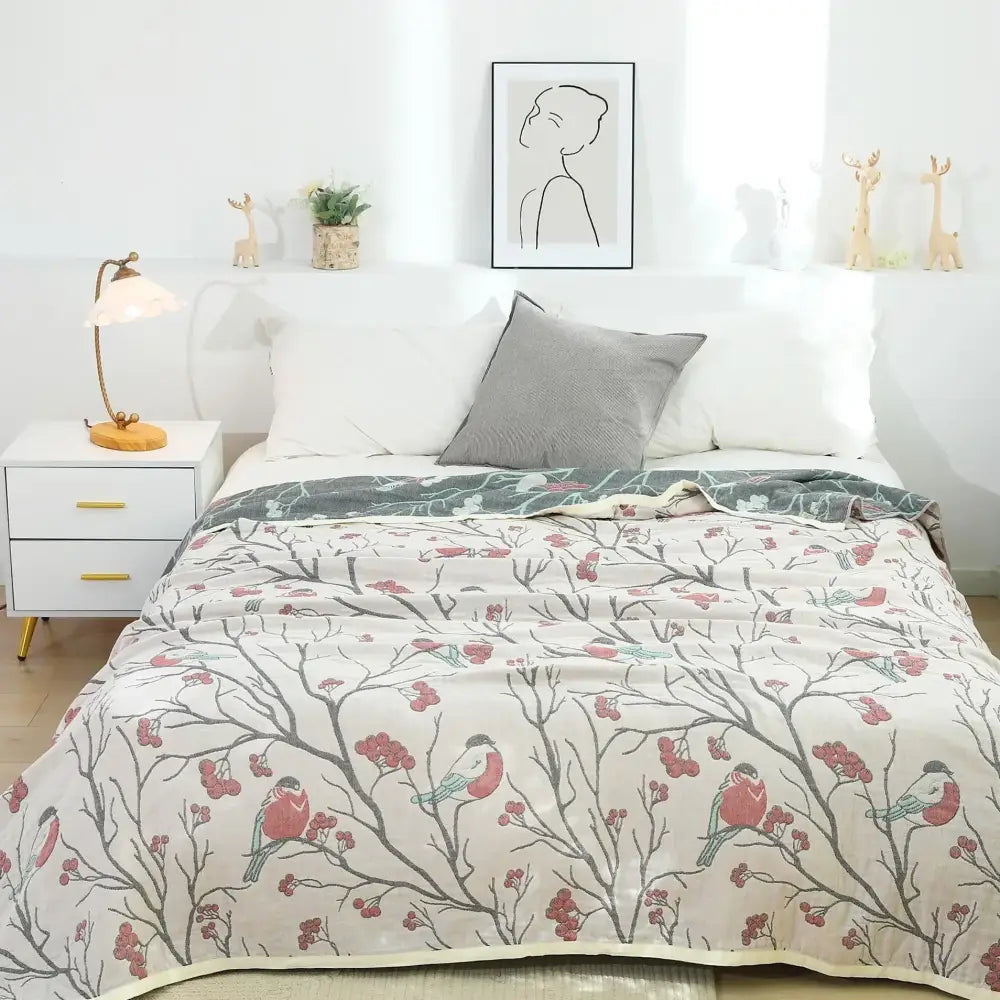 A soft cream cotton gauze summer blanket with gray branches red berries and pink and blue birds pattern