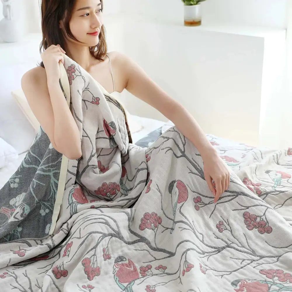 A soft light gray cotton gauze summer blanket with pink blossoms and birds on slender branches for bedroom use