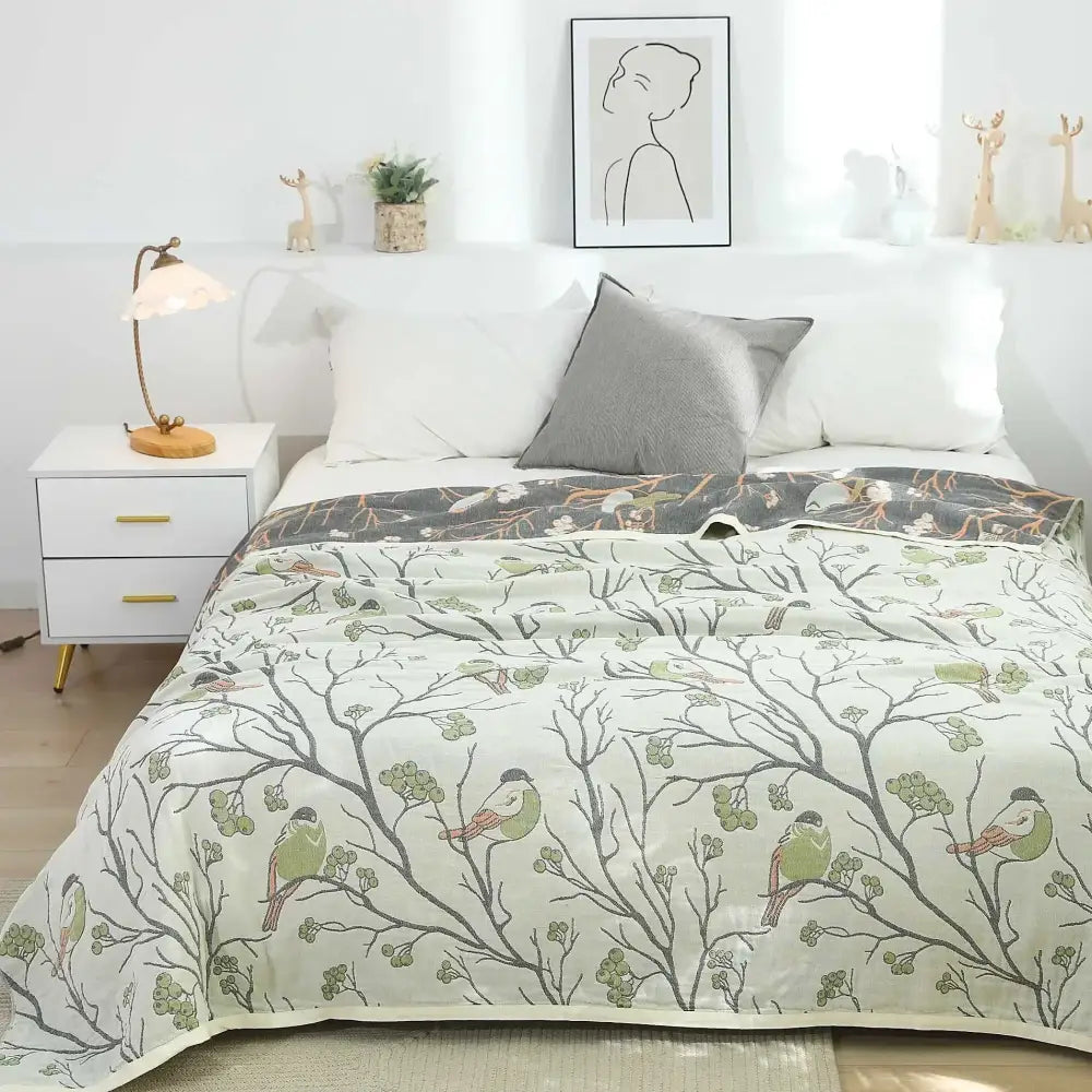 A soft light green and gray patterned cotton gauze summer blanket with birds on branches, ideal as a bedroom throw