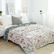 A cream cotton gauze summer blanket with quilted texture featuring red birds on dark gray branches and berries