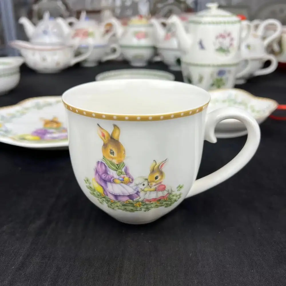 A white porcelain teacup with gold-dotted rim and illustrated rabbits from a floral scalloped tulip dinnerware set
