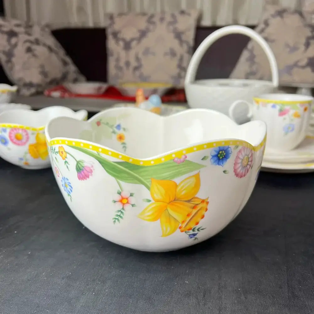 A white porcelain dinnerware set bowl with scalloped rim and vibrant floral patterns including yellow daffodils and pink blossoms