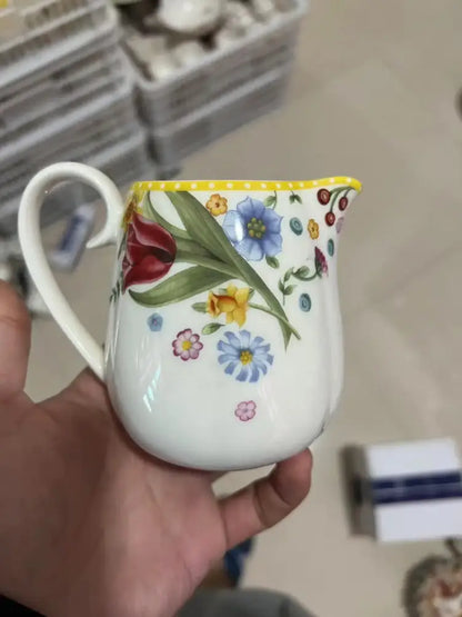 A white ceramic pitcher with yellow rim and colorful floral design from a floral scalloped white porcelain tulip dinnerware set