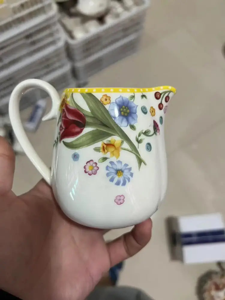 A white ceramic pitcher with yellow rim and colorful floral design from a floral scalloped white porcelain tulip dinnerware set