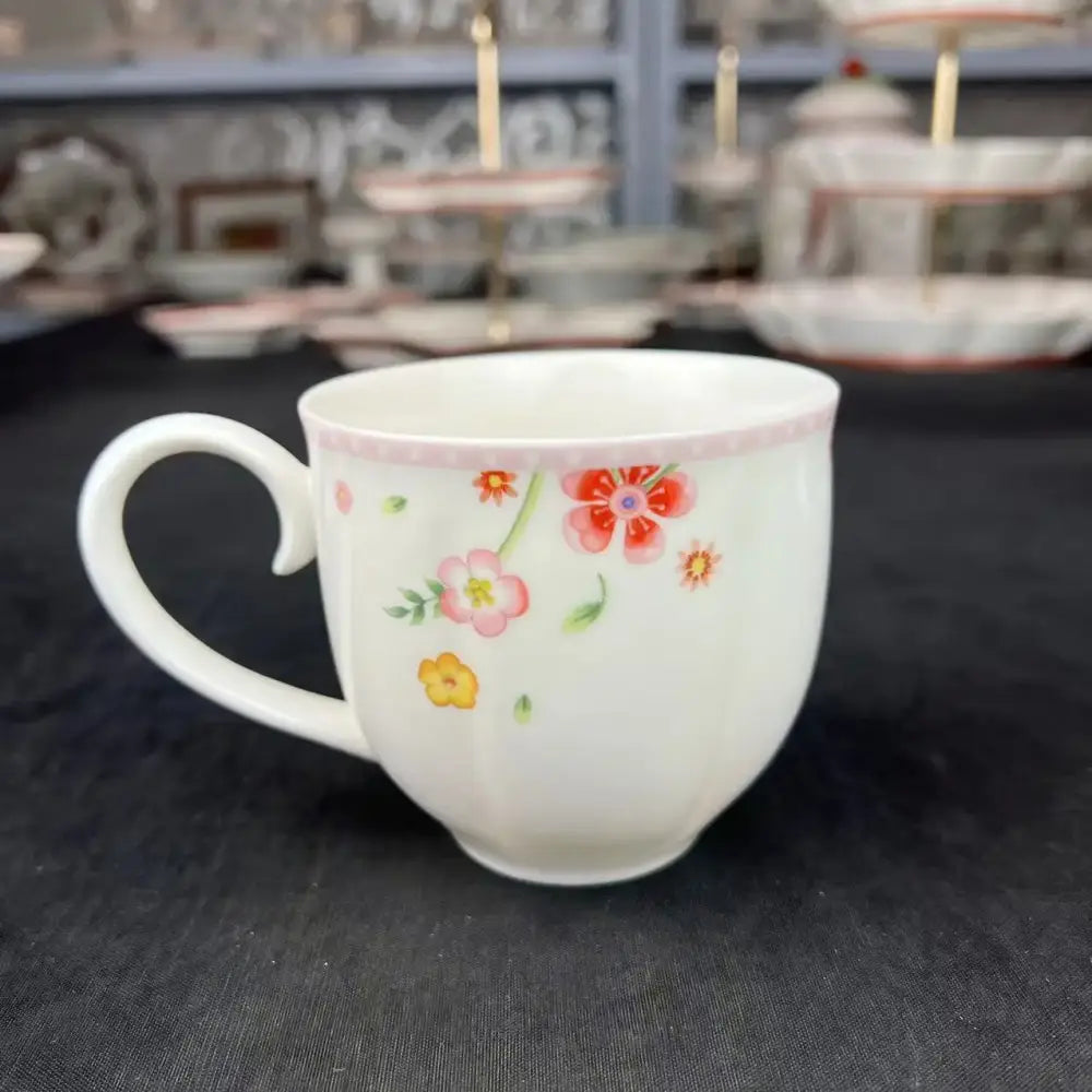 A white ceramic mug with delicate pink and yellow floral patterns and a pink rim from a tulip dinnerware set