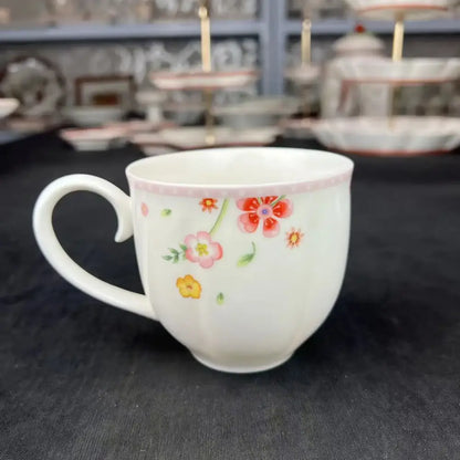 A white ceramic mug with pink and yellow floral patterns and a pink rim from a tulip dinnerware set