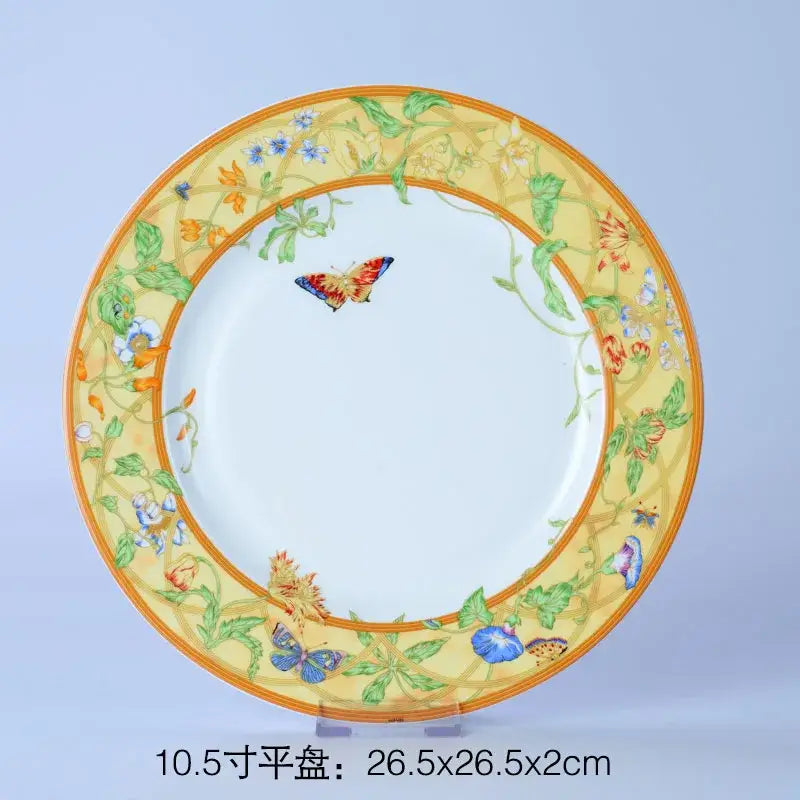 A decorative bone dinnerware set plate with yellow border green vines blue orange flowers and a colorful butterfly design