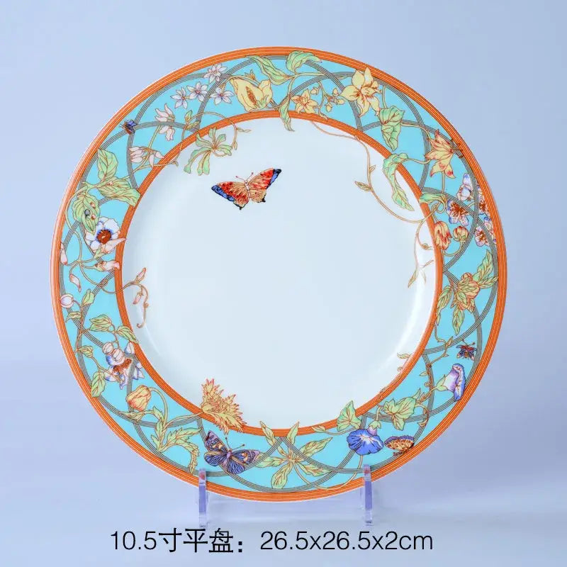 A decorative bone dinnerware set plate with a vibrant turquoise border floral and butterfly motifs and orange rim