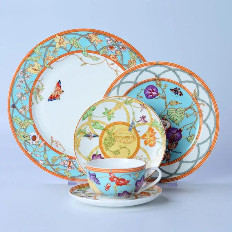 A vibrant turquoise and gold bone dinnerware set with floral and butterfly motifs and a bold orange rim