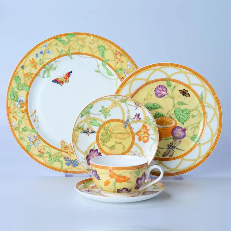 A vibrant yellow bone dinnerware set with floral and butterfly motifs in orange purple and green accents