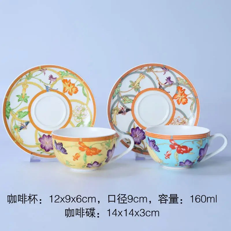 Two ornate porcelain coffee cups in yellow-orange and light blue with matching saucers from a bone dinnerware set