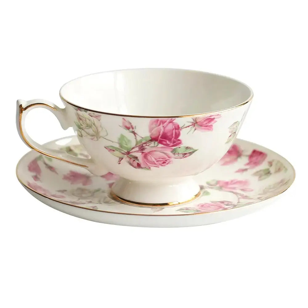 A delicate white bone china tea cup set with pink rose blossoms green leaves and gold rim for elegant dining