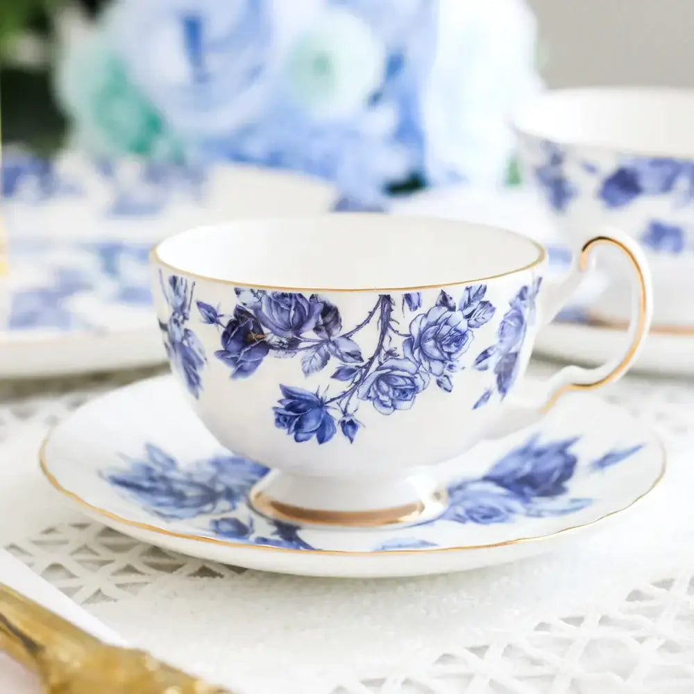 A delicate white bone china tea cup set with blue rose patterns and gold rim on matching saucer for dining room use
