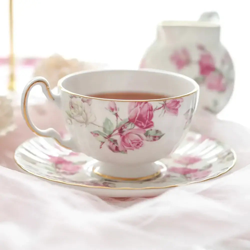 A delicate white bone china tea cup with pink rose patterns and gold trim in a floral tea cup set for dining room use