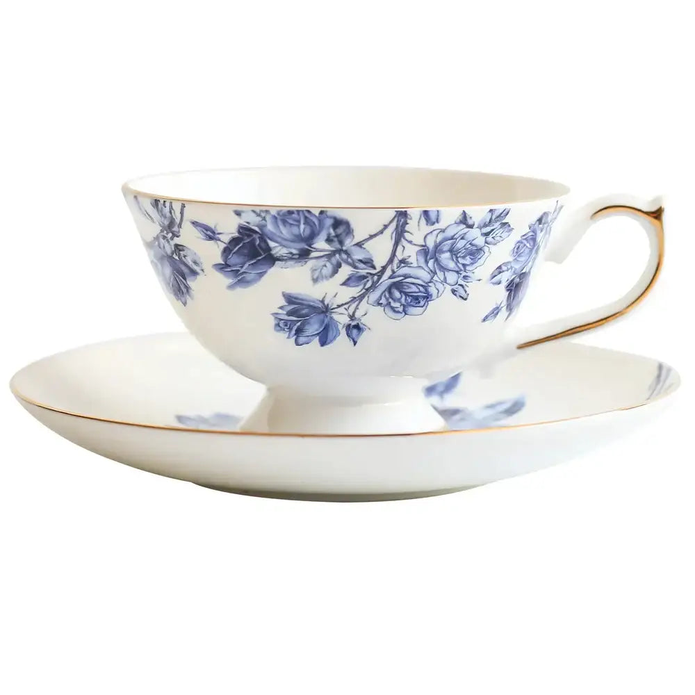 A delicate white bone china tea cup set with blue rose blossoms and gold rim for elegant dining room drinkware