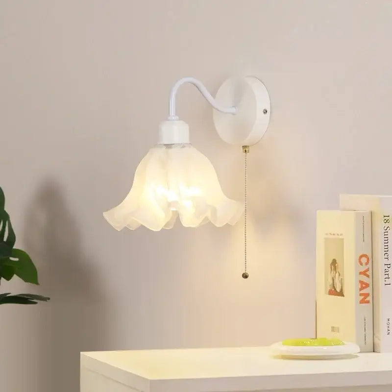 White wall sconce with translucent petal-shaped glass shade and curved metal arm featuring pull chain switch